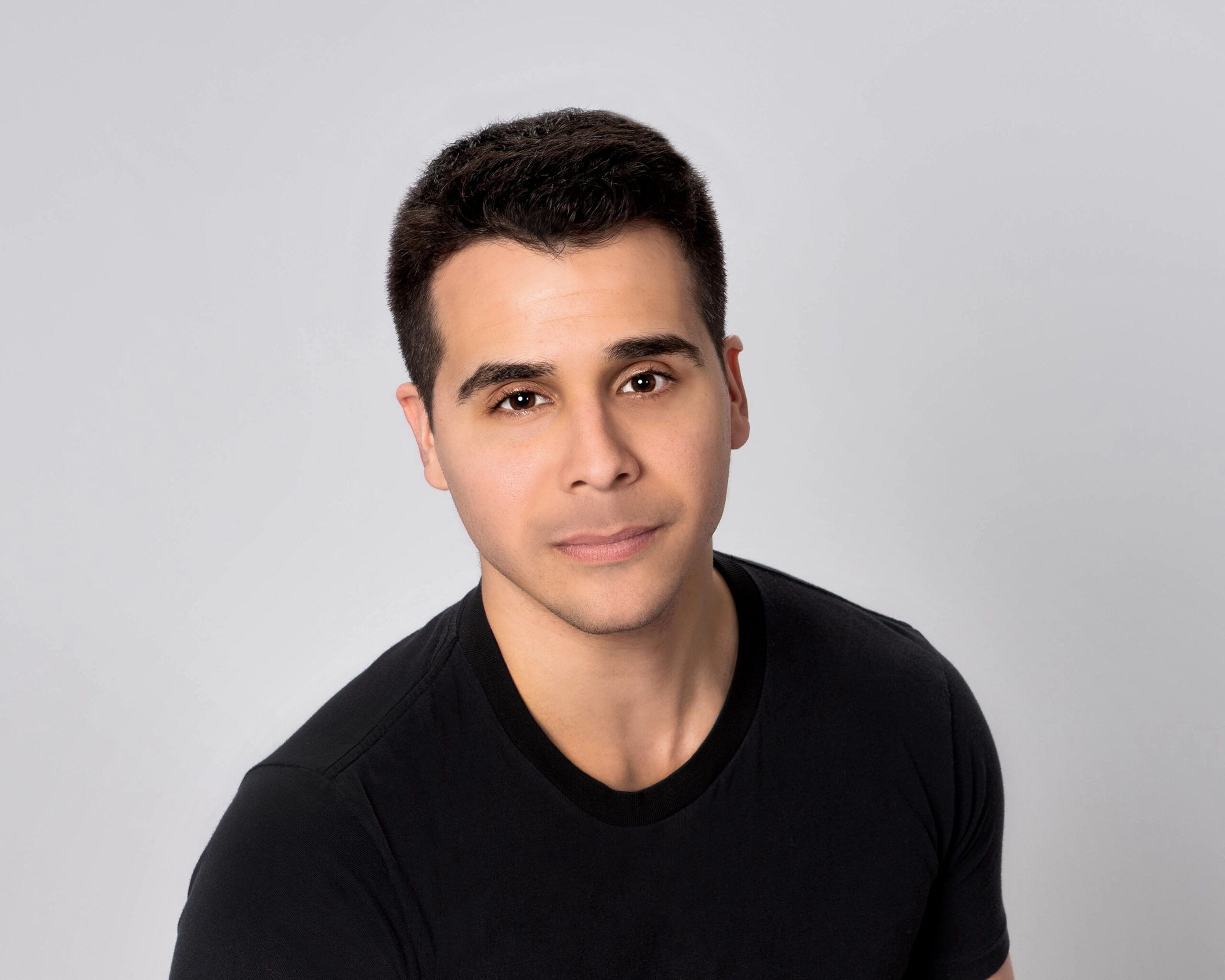 male voiceover coach Tom Aglio, wearing a black shirt and standing in front of a gray background