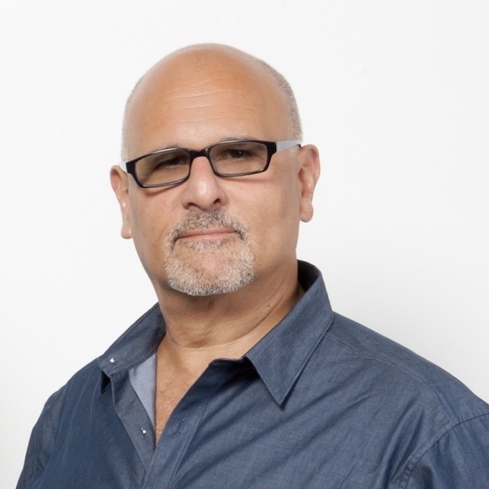 male voiceover coach Bruce Kronenberg wearing blue button down shirt standing in front of a white background