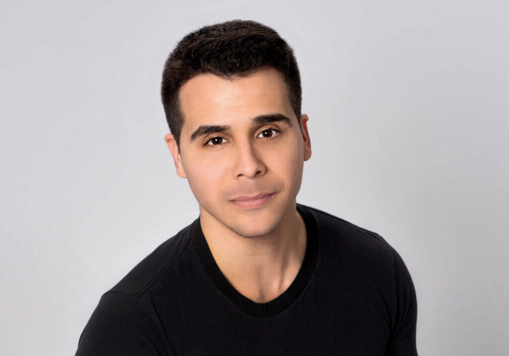male voiceover coach Tom Aglio, wearing a black shirt and standing in front of a gray background