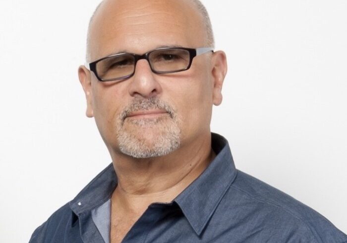 male voiceover coach Bruce Kronenberg wearing blue button down shirt standing in front of a white background