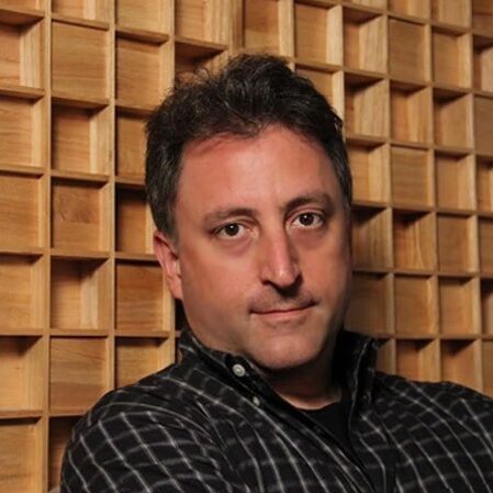 male voiceover engineer Bryant Falk, wearing black plain button down shirt standing in front of wood wall